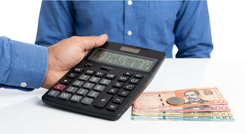 Fotografía de primer plano de una mano sosteniendo una calculadora física sobre pesos dominicanos, representando el cálculo del anticipo de la DGII.